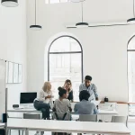 Eine Gruppe von Mitarbeiter:innen in einem hellen, stilvollen Büro bei einer Teamdiskussion. Dies illustriert, wie unsere Dienstleistungen Bewerber:innen dabei unterstützen, in einer professionellen Arbeitsumgebung Fuß zu fassen und wertvolle Teamarbeitserfahrung zu sammeln.