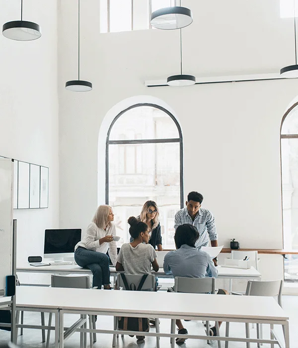 Eine Gruppe von Mitarbeiter:innen in einem hellen, stilvollen Büro bei einer Teamdiskussion. Dies illustriert, wie unsere Dienstleistungen Bewerber:innen dabei unterstützen, in einer professionellen Arbeitsumgebung Fuß zu fassen und wertvolle Teamarbeitserfahrung zu sammeln.