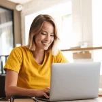 Fröhliche weibliche Führungskraft, die einen Laptop benutzt und lächelt, während sie in einem Unternehmen sitzt