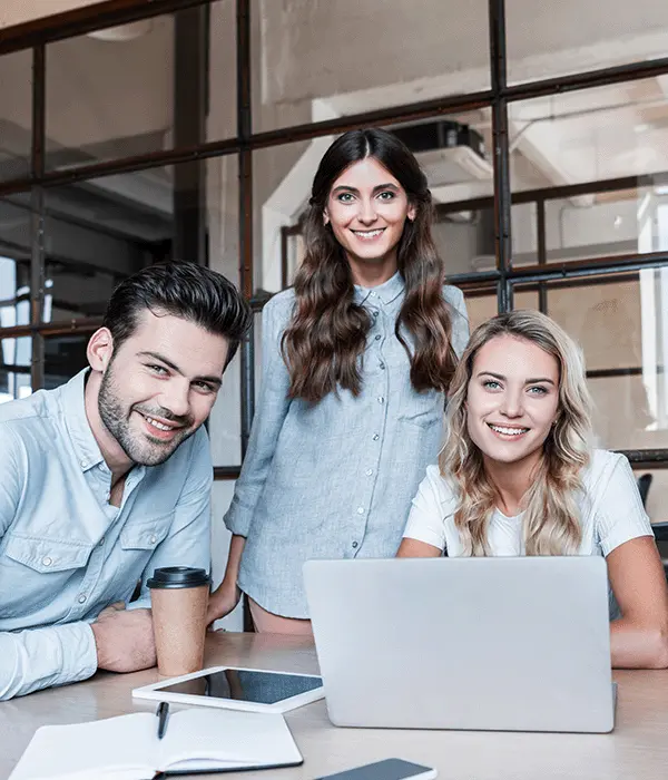glückliche junge Geschäftskollegen, die im Büro mit Geräten arbeiten und in die Kamera lächeln