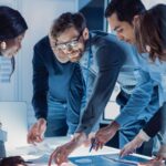 eam bespricht technische Unterlagen an einem Tisch – Szene im beruflichen Kontext, wie sie im Jobportal für technische und ingenieurbezogene Jobs erscheint.