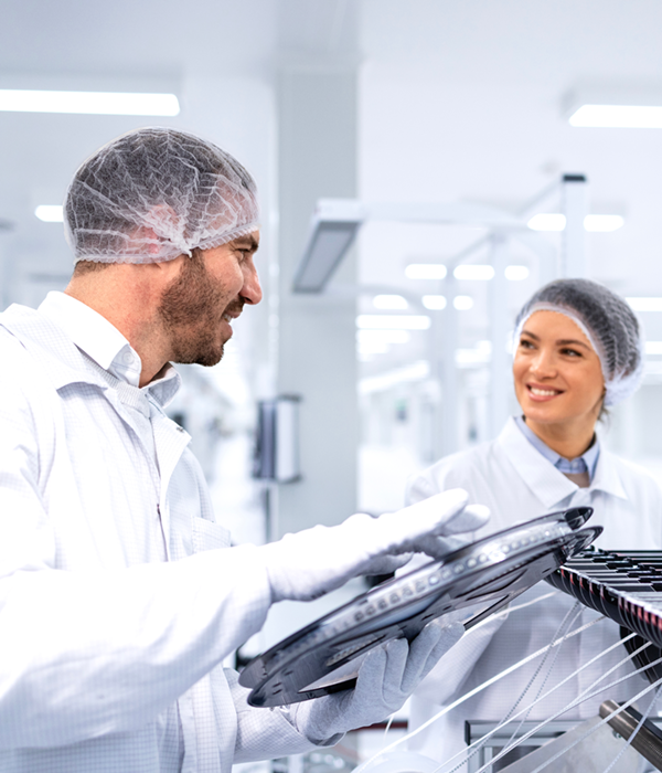 Zwei Mitarbeitende in Reinraumkleidung arbeiten gemeinsam an Bauteilen in einer modernen Produktionsumgebung der Halbleiterherstellung.