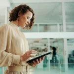 HR-Mitarbeiterin im Recruiting-Prozess prüft Bewerbungsunterlagen auf einem Tablet in einem modernen Büro.