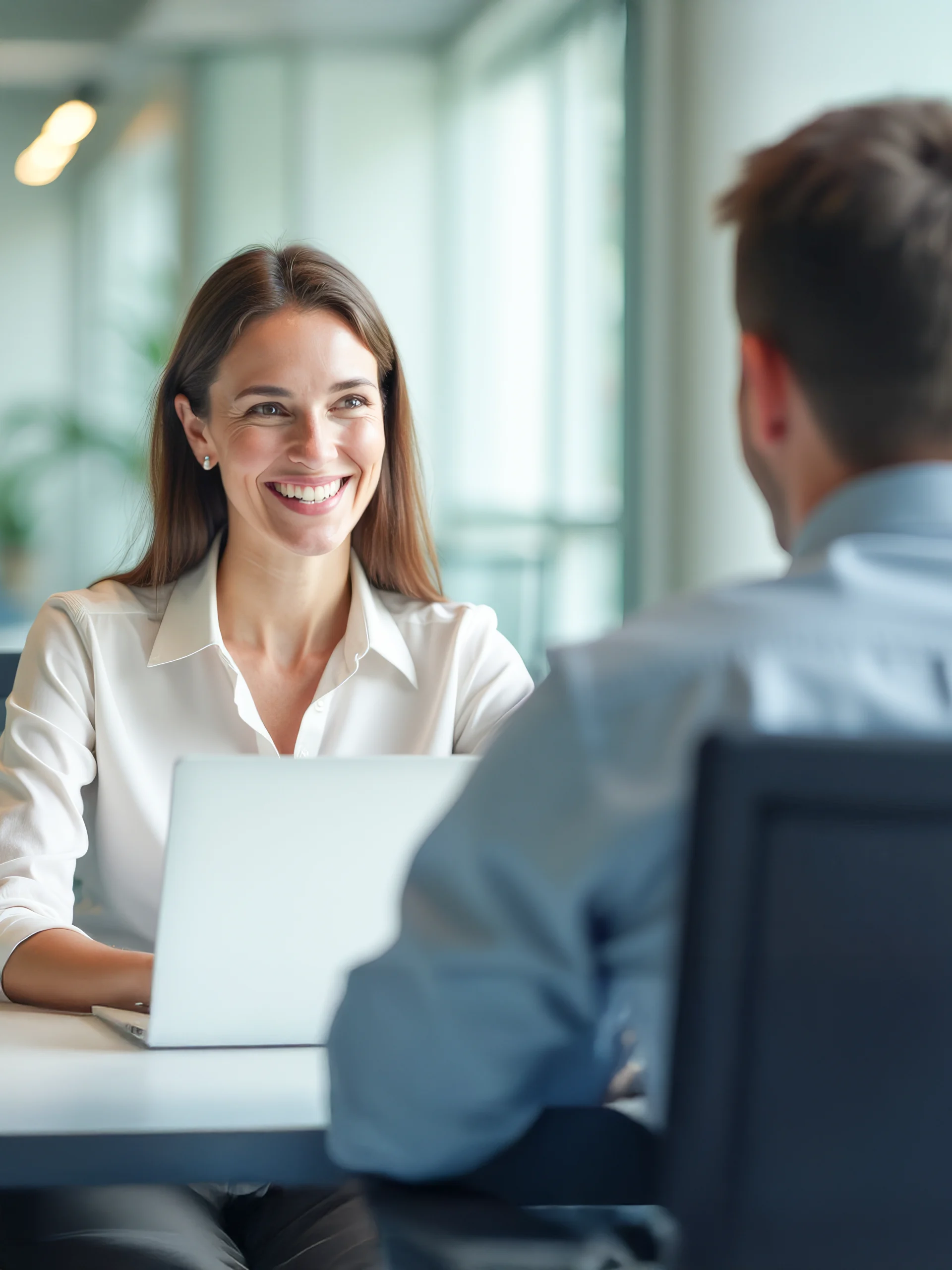 Junge Berufseinsteigerin im freundlichen Gespräch mit einem Kollegen im modernen Büro. Beide sitzen sich gegenüber und tauschen sich über Aufgaben und Einstiegsmöglichkeiten aus.