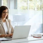 Person arbeitet konzentriert am Laptop in einem modernen Büro. Auf dem Schreibtisch liegen Unterlagen und ein Smartphone. Professionelles Arbeitsumfeld als Symbol für einen strukturierten Recruiting-Prozess.