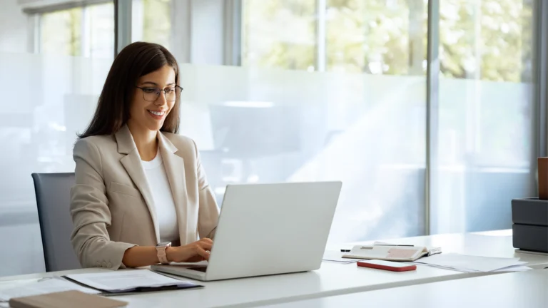 Person arbeitet konzentriert am Laptop in einem modernen Büro. Auf dem Schreibtisch liegen Unterlagen und ein Smartphone. Professionelles Arbeitsumfeld als Symbol für einen strukturierten Recruiting-Prozess.