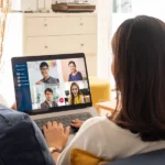Flexible Arbeitsmodelle im Einsatz: Eine Person arbeitet von zu Hause aus auf dem Sofa und ist per Videomeeting mit dem Team verbunden.