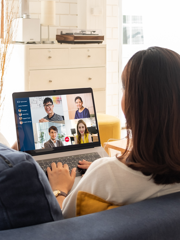 Flexible Arbeitsmodelle im Einsatz: Eine Person arbeitet von zu Hause aus auf dem Sofa und ist per Videomeeting mit dem Team verbunden.