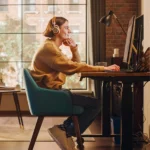 Person arbeitet zu Hause im Homeoffice an einem Schreibtisch, trägt Kopfhörer und nutzt flexible Arbeitszeiten. Die Szene zeigt modernes, flexibles Arbeiten: Laptop, ergonomischer Arbeitsplatz und entspannte Atmosphäre – ein Beispiel für flexible Arbeitsmodelle und selbstbestimmtes Arbeiten.
