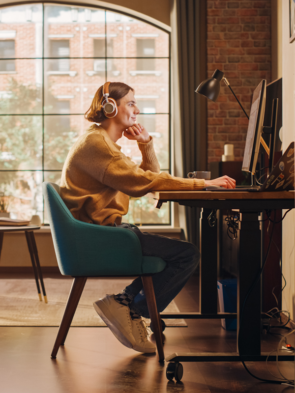 Person arbeitet zu Hause im Homeoffice an einem Schreibtisch, trägt Kopfhörer und nutzt flexible Arbeitszeiten. Die Szene zeigt modernes, flexibles Arbeiten: Laptop, ergonomischer Arbeitsplatz und entspannte Atmosphäre – ein Beispiel für flexible Arbeitsmodelle und selbstbestimmtes Arbeiten.