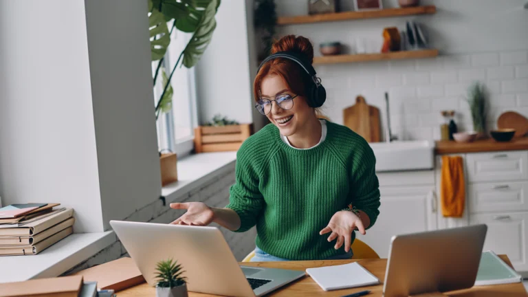 Junge Frau arbeitet im Homeoffice an einem Laptop, trägt Kopfhörer und lächelt während eines Online-Meetings – Beispiel für flexible Arbeitsmodelle und ortsunabhängiges Arbeiten.