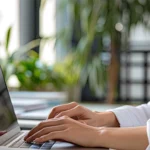 Hände einer Person, die konzentriert an einem Laptop in einem hellen Büro mit Pflanzen arbeitet; ruhiger Arbeitsplatz, der verdeutlicht, wie wichtig Fokus, passende Arbeitsumgebung und persönliche Freiräume bei der Jobwahl sind.