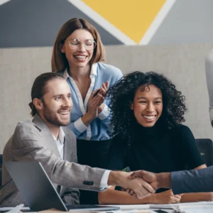 Drei Personen sitzen in einem modernen Büro bei einem Bewerbungsgespräch. Sie lächeln und geben einer vierten Person außerhalb des Bildausschnitts die Hand – ein Zeichen dafür, dass der Bewerbungsprozess erfolgreich abgeschlossen wurde.