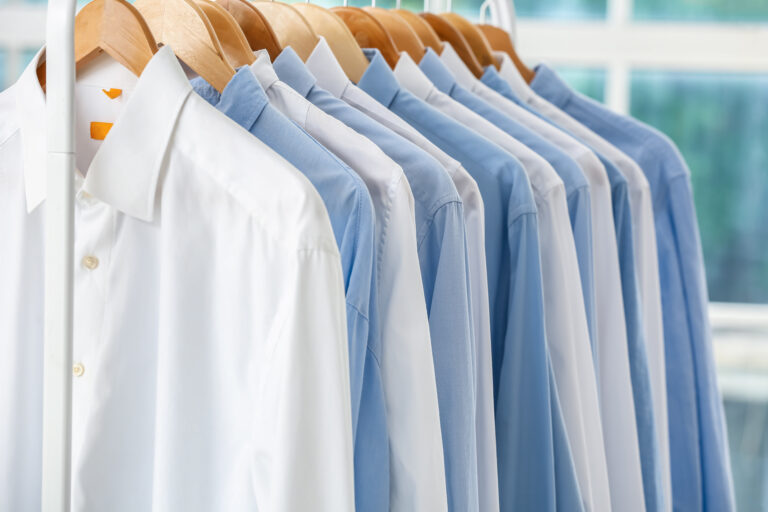 Ordentlich aufgereihte hellblaue und weiße Hemden in einem Schrank – klassische Kleidungsauswahl für den Business-Look beim Vorstellungsgespräch.