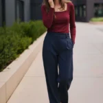 Frau in einem Business-Casual-Outfit für ein Vorstellungsgespräch, bestehend aus einem bordeauxroten, langärmligen Oberteil mit eckigem Ausschnitt, dunkelblauer Bundfaltenhose und schwarzen Absatzschuhen. Das Outfit wirkt elegant und stilvoll, eignet sich besonders für Bewerbungsgespräche in modernen oder kreativen Branchen.