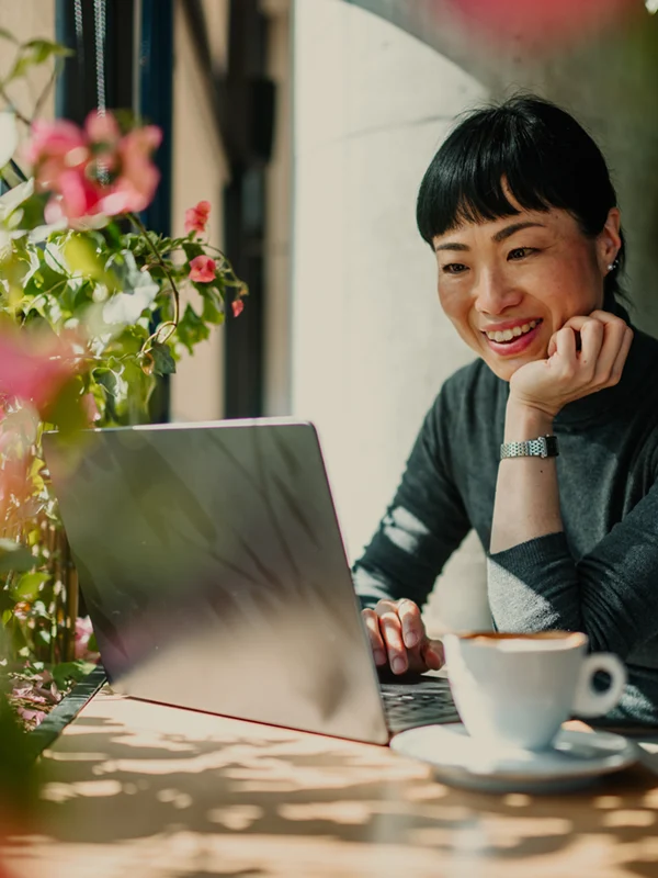 Eine Frau arbeitet entspannt mit ihrem Laptop in einem Café im Grünen, trinkt Kaffee und wirkt zufrieden – ein Moment, der zeigt, wie wichtig bei der Jobwahl persönliche Prioritäten wie Sinn, Weiterentwicklung und ein Arbeitsumfeld sind, das zum eigenen Leben passt.