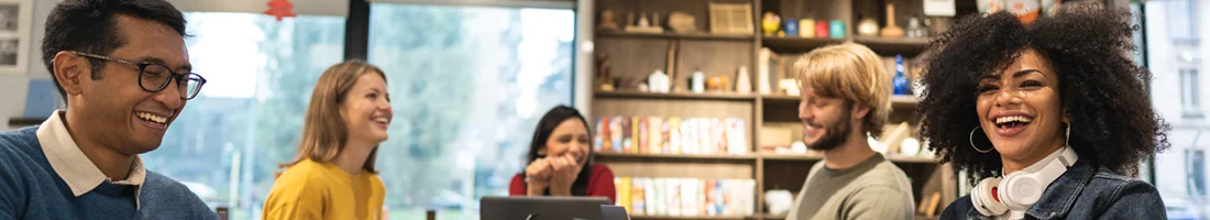 Mehrere Personen sitzen gemeinsam in einem modernen Büro, lachen und unterhalten sich. Eine lebendige Büroszene, die unterschiedliche Stilrichtungen und Outfits im Arbeitsumfeld zeigt.