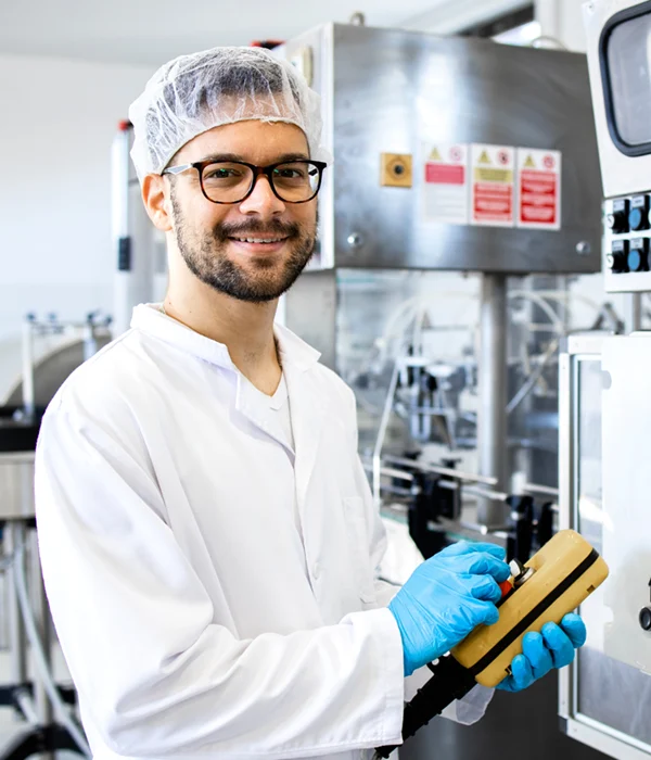 Mitarbeiter in der Pharmaindustrie trägt Laborkittel, Haarnetz und Handschuhe und bedient eine Maschine im Reinraumbereich.