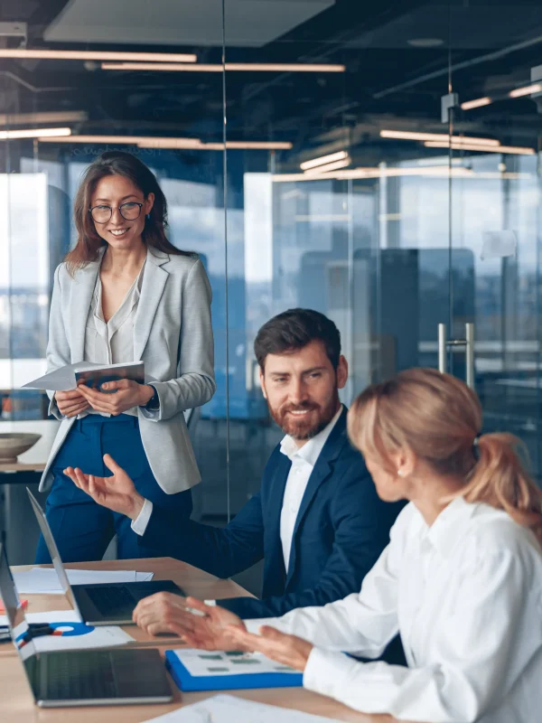 Ein Team von Fachleuten, das in einem modernen Büro eine Besprechung über Steuerberatung und Finanzwesen durchführt, wobei eine Frau im Vordergrund ein Dokument hält und lächelt.
